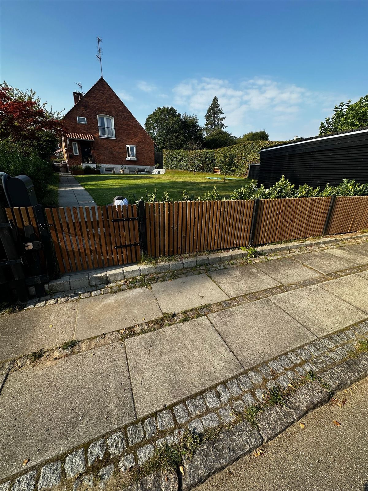 Stakit med havelåge i thermofyr langs fortov foran villa